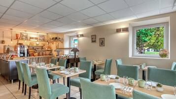Un restaurante con zona de bar, sillas tapizadas de verde y vista a vegetación a través de una ventana.