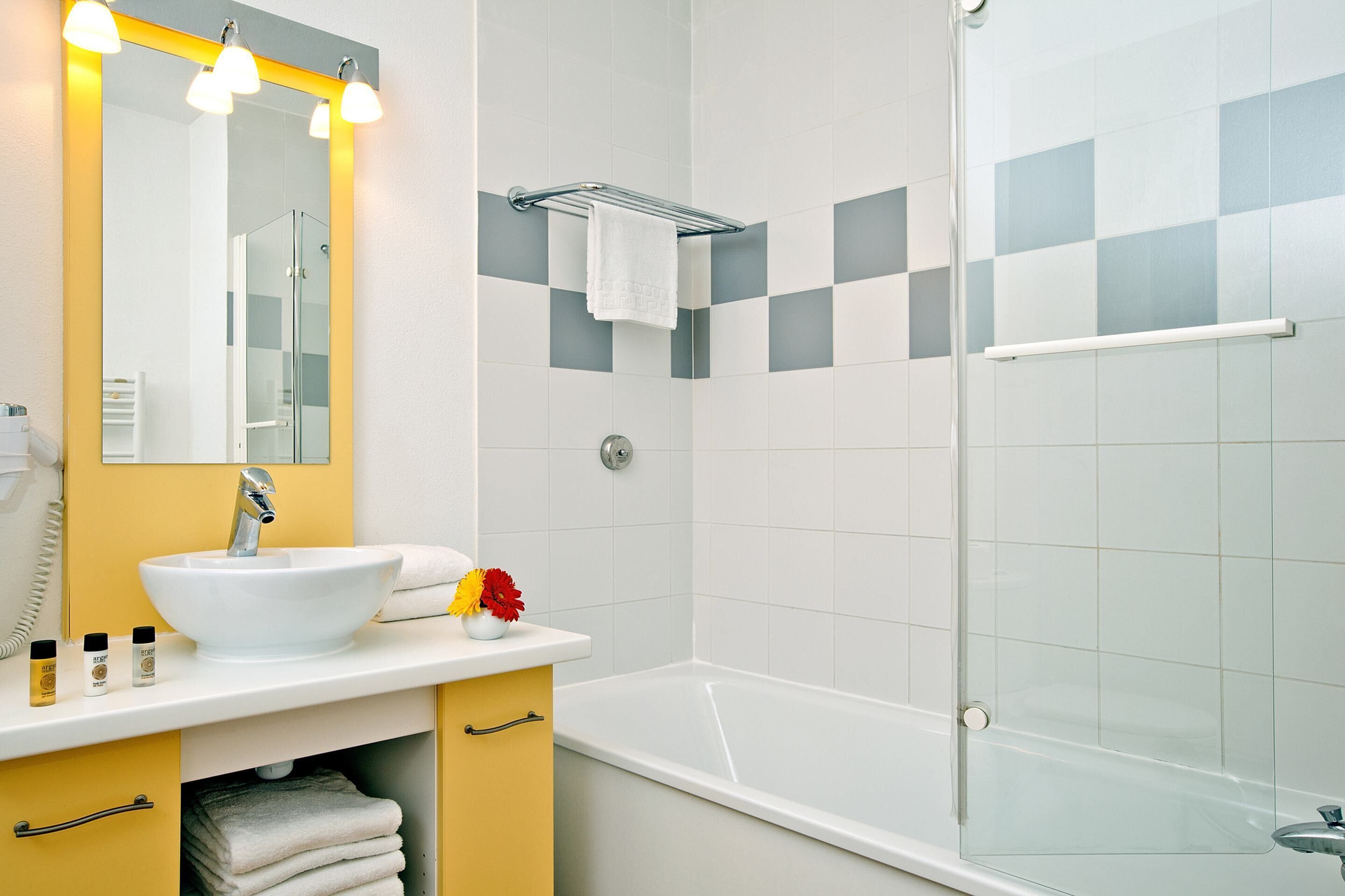 Un bagno con lavandino bianco, mobile giallo, cabina doccia in vetro e specchio con illuminazione.