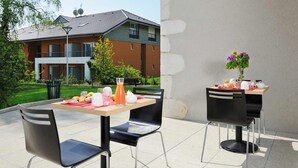 Un área de comedor al aire libre con dos mesas, sillas negras y una variedad de comida y bebidas.