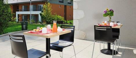 Un área de comedor al aire libre con dos mesas, sillas negras y una variedad de comida y bebidas.