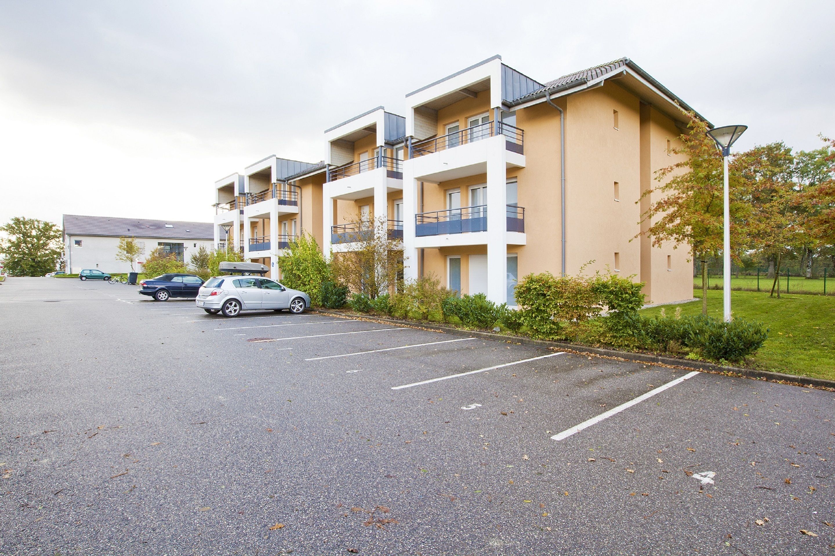 A multi-story residential building with balconies, a parking lot, and a street lamp.