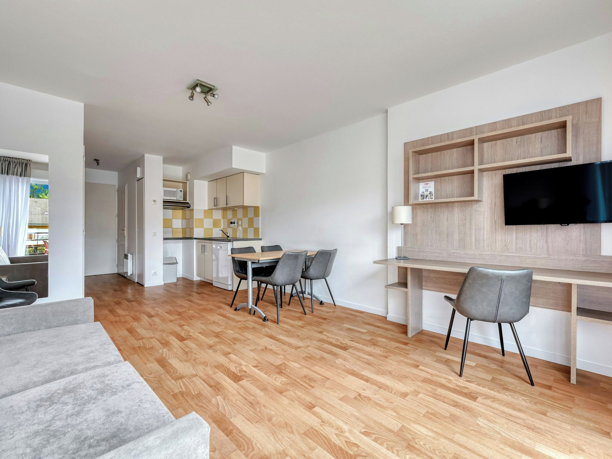 A modern apartment with a dining area, kitchen, and a TV mounted on the wall.