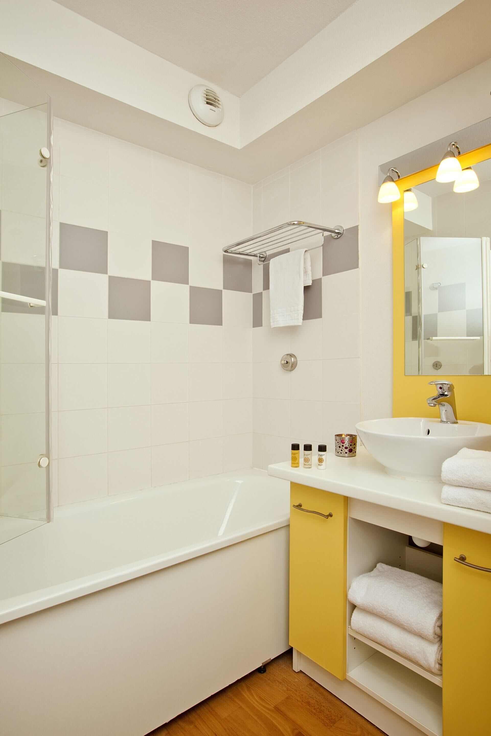 Un baño moderno con una bañera blanca, un tocador amarillo con espejo y una zona de ducha con azulejos.