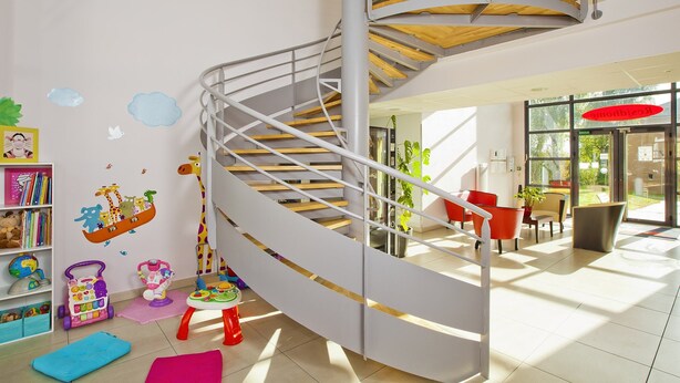 Un interior moderno con una escalera de caracol, una zona de juegos para niños y un espacio de descanso con vistas al exterior.