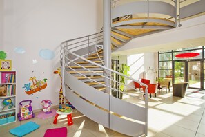 Un interior moderno con una escalera de caracol, una zona de juegos para niños y un espacio de descanso con vistas al exterior.