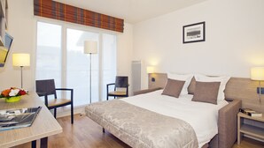 Habitación de hotel con una cama grande, dos sillas, un escritorio con lámpara y una ventana con vistas.