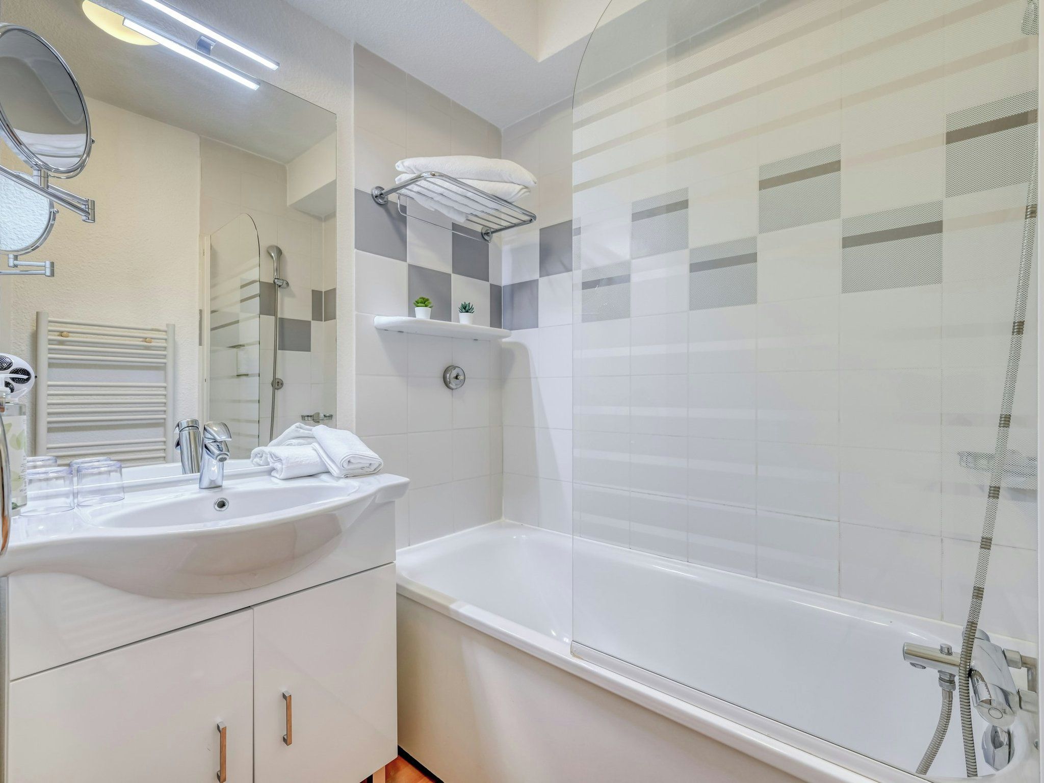 A bathroom with a sink, mirror, towel rack, and a shower area.