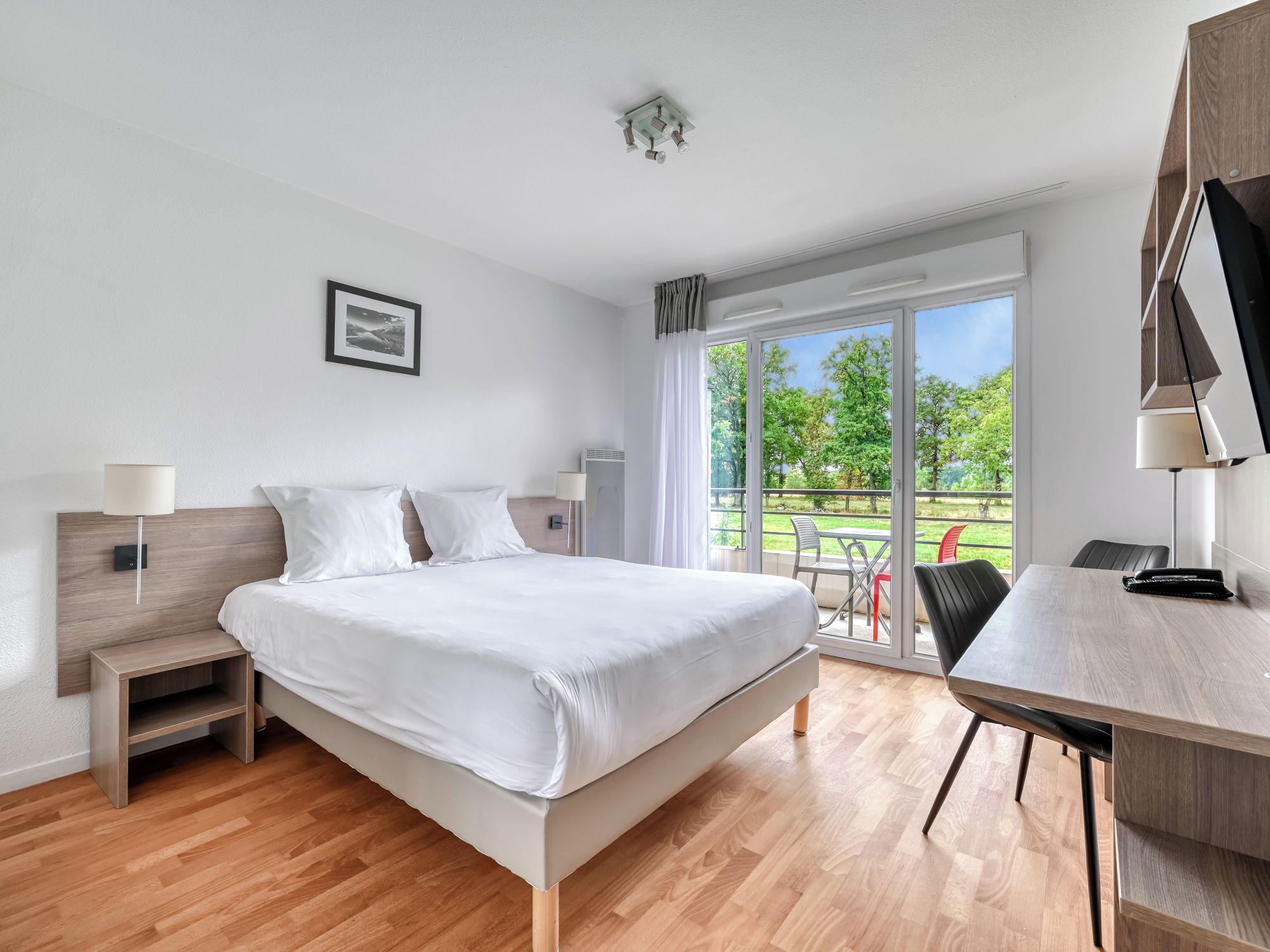 Un dormitorio moderno con una cama grande, mesitas de noche, un escritorio y vistas al exterior.