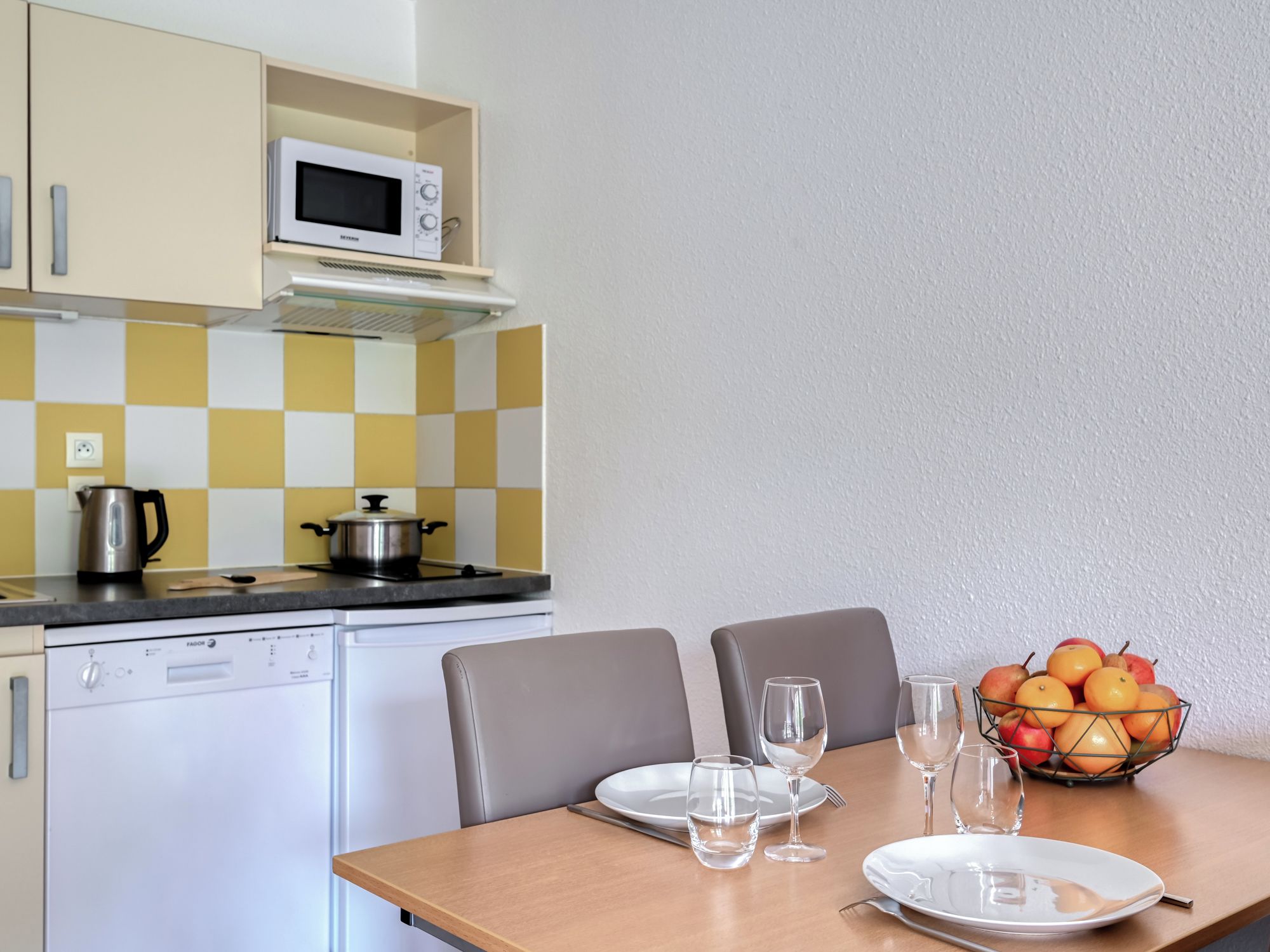 Una cucina compatta con forno a microonde, fornello e una ciotola di frutta sul tavolo.