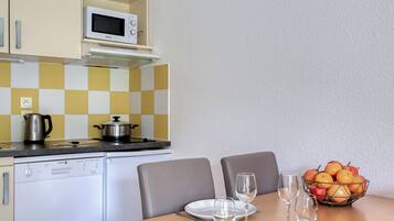 Una cucina compatta con forno a microonde, fornello e una ciotola di frutta sul tavolo.