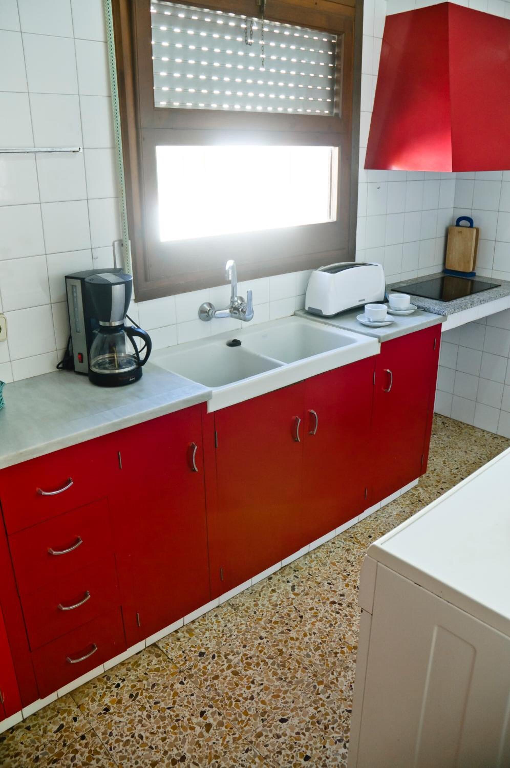 A kitchen with red cabinets, a white countertop, a coffee maker, a toaster, and a sink.