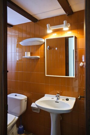A bathroom with orange tiled walls, a white sink, a mirror, and a toilet. - RVApartaments Villas Piscis (Torroella de Montgrí)