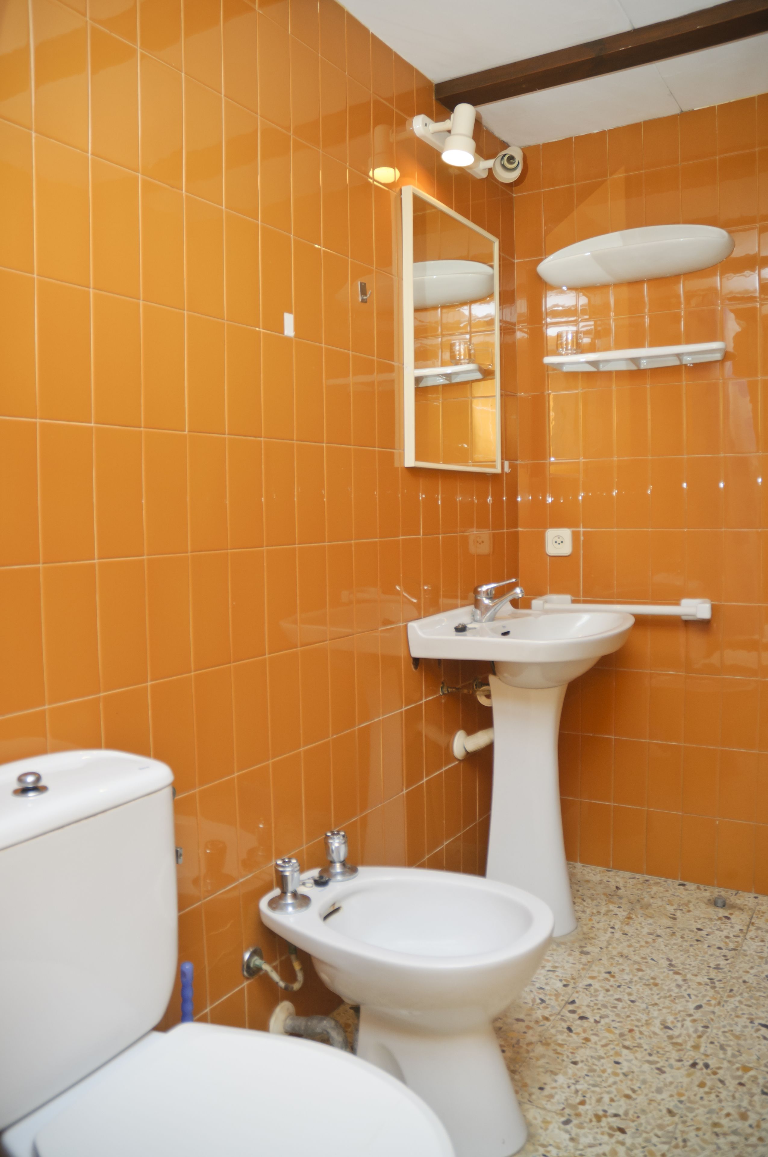 A bathroom with orange tiled walls, a white sink, a mirror, and a toilet.