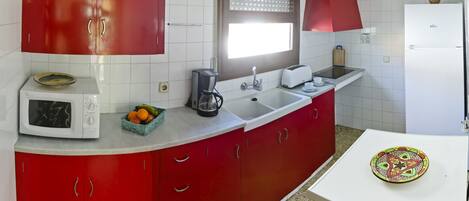 Una cocina con armarios rojos, un microondas blanco, una cafetera y un refrigerador.