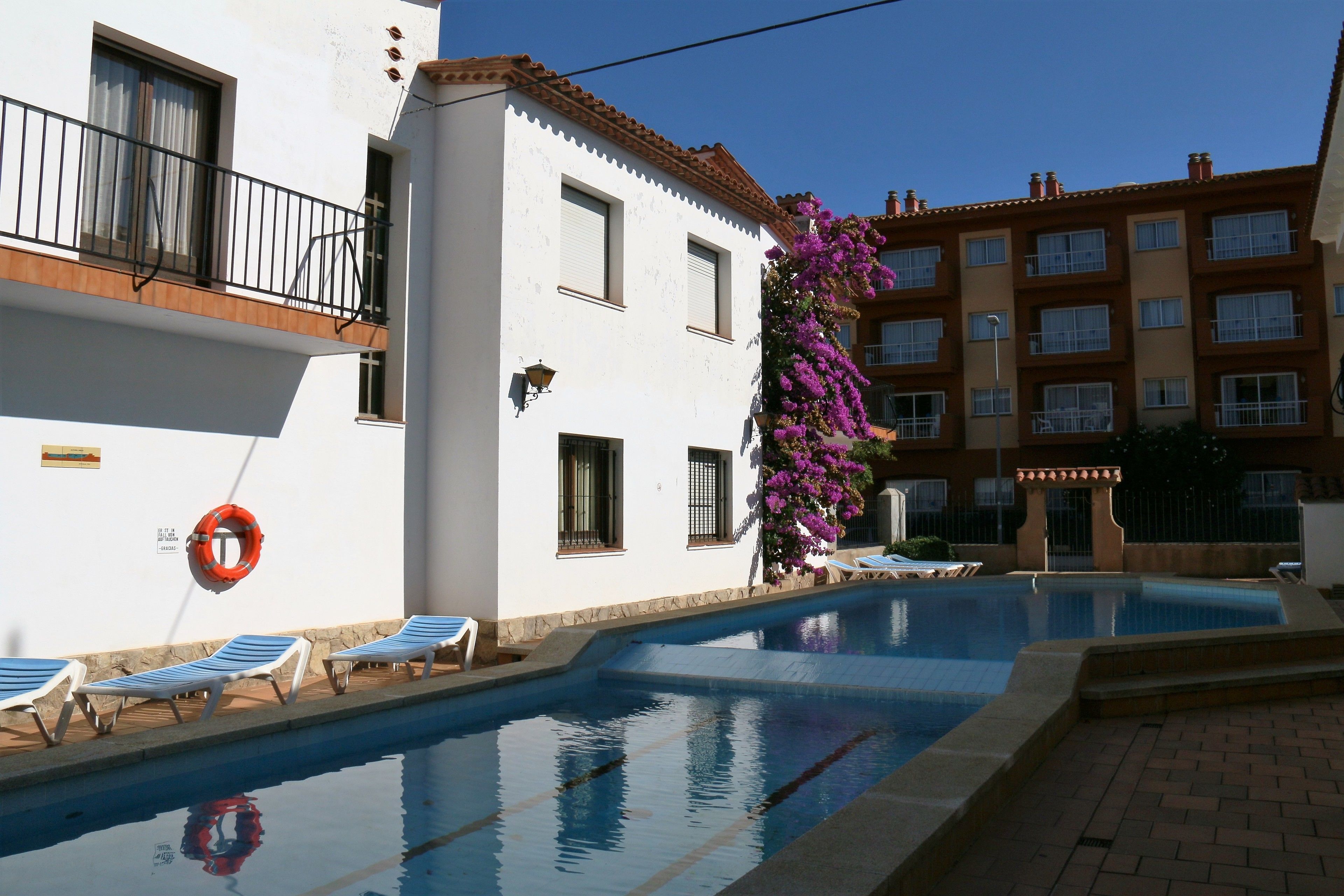 A swimming pool with lounge chairs, a lifebuoy, and a building with balconies and windows.