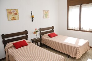 A room with two beds, each with striped bedding and a red pillow. There is a small table with a vase of flowers between the beds. - RVApartaments Villas Piscis (Torroella de Montgrí)