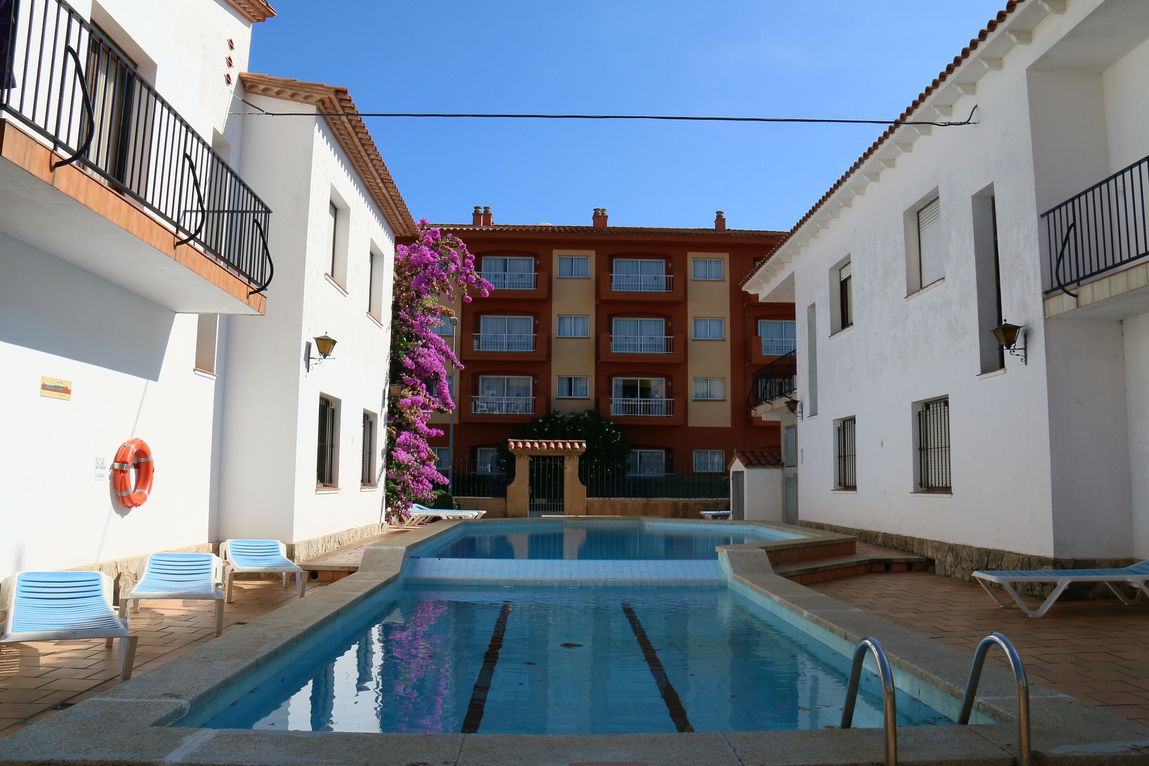 A swimming pool with lounge chairs, a lifebuoy, and a building with balconies and windows.