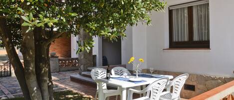 An outdoor dining area with a table and chairs, a tree, and a building with a window.