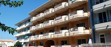 A multi-story residential building with balconies, a central entrance, and a parking area.