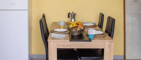 Una mesa de comedor con sillas, una cesta de frutas y una cafetera.