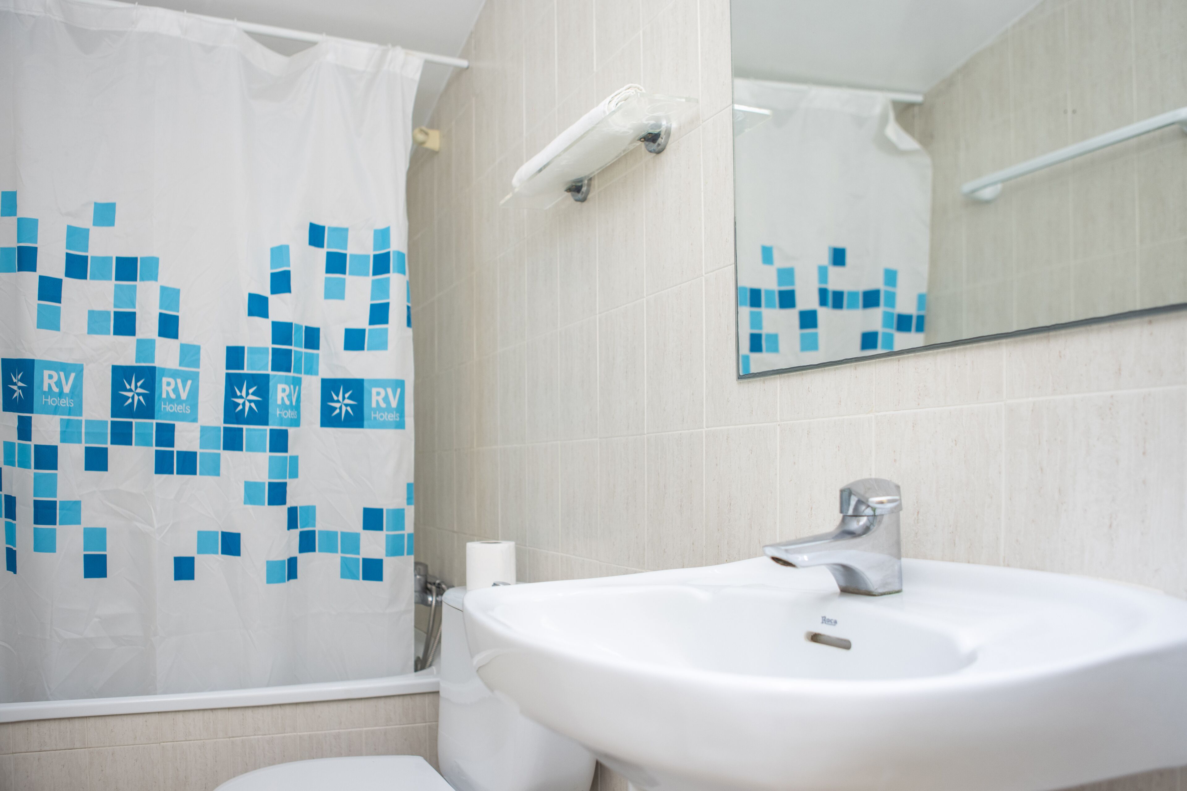 Un baño con lavamanos blanco, un espejo y cortina de ducha con estampado azul.