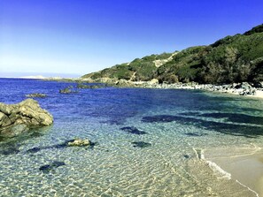 A coastal beach with clear shallow waters, rocky outcrops, and a sandy shoreline. - Bed Sandalia (Badesi)