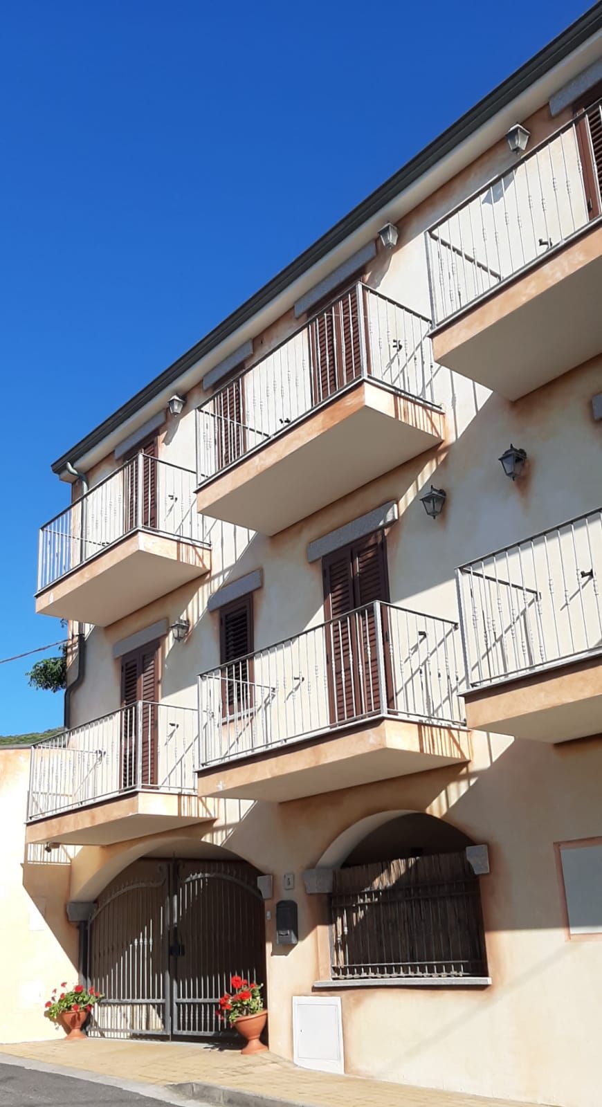 Un edificio a più piani con balconi, un ingresso carrabile e piante in vaso.