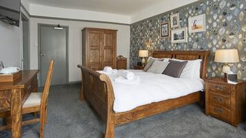 Une chambre à coucher avec un lit en bois, deux tables de chevet avec des lampes, une armoire en bois, un bureau avec une chaise et un sol recouvert d’une moquette.