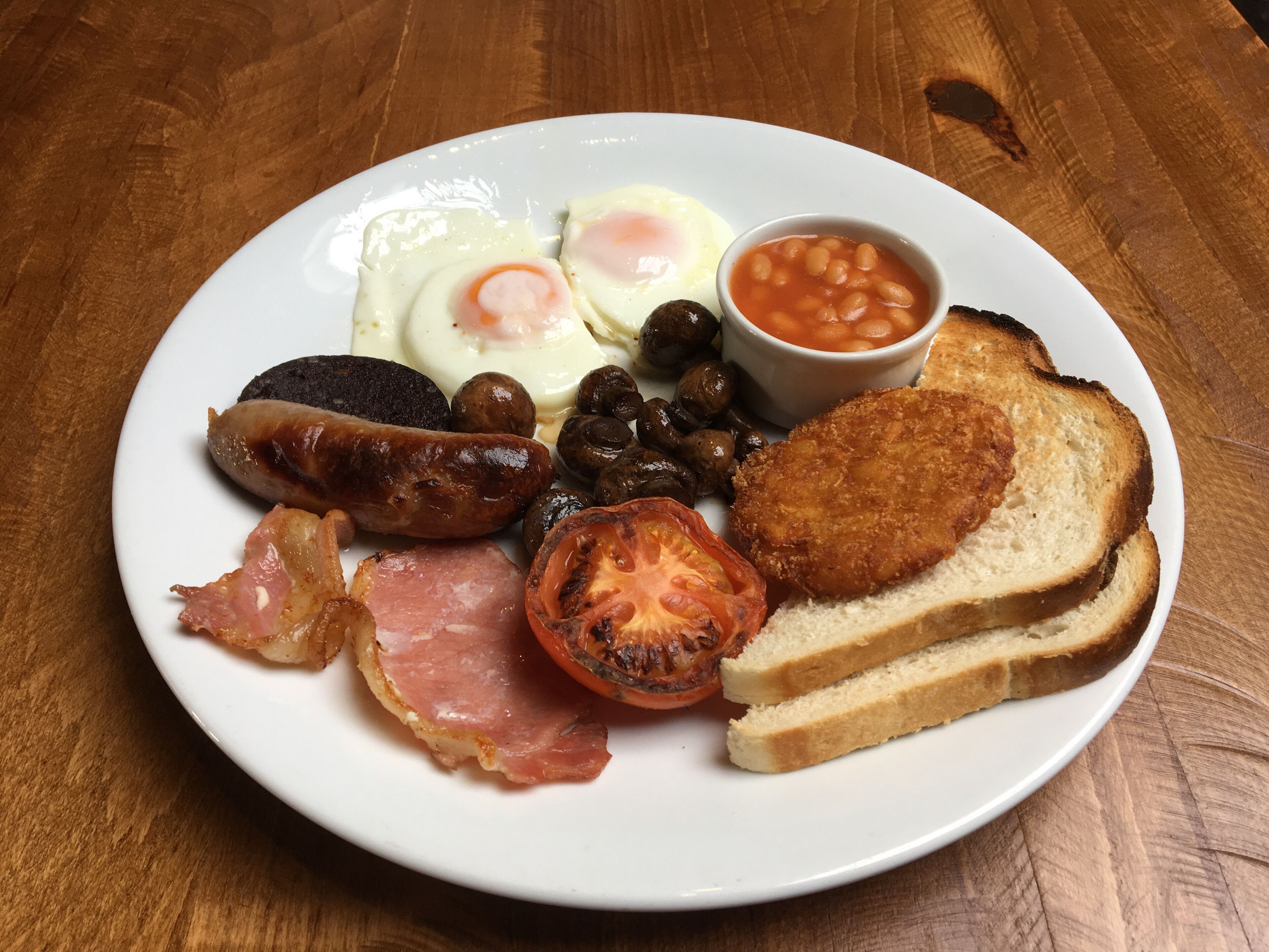 Ein Teller mit Frühstücksessen, darunter Eier, Würstchen, Pilze, Speck, Toast und Bohnen.