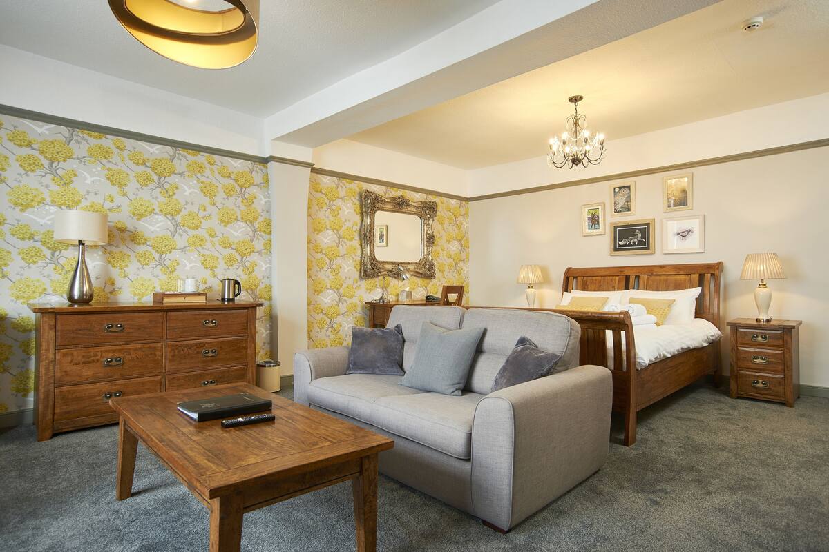 A bedroom with a sofa, a wooden bed, a nightstand, a dresser, and a chandelier.