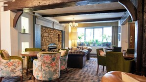 A cozy room with a stone wall, a wooden ceiling, and a patterned carpet. There are floral armchairs, a leather sofa, and a dining table with chairs. - Angel Inn Hotel (Pershore)