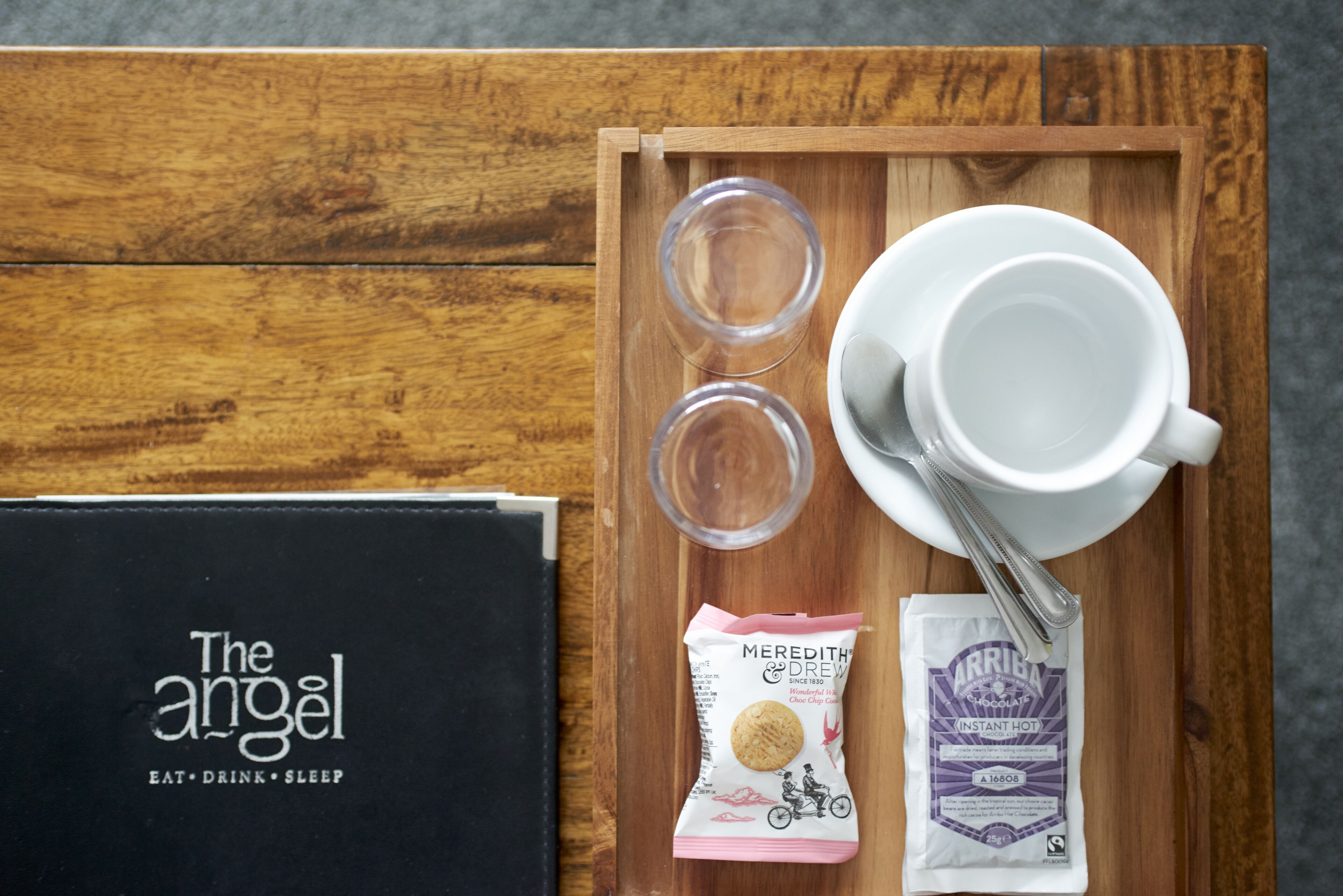 Un plateau en bois sur lequel se trouvent une tasse blanche, deux verres transparents, un paquet de biscuits et un paquet de café instantané.