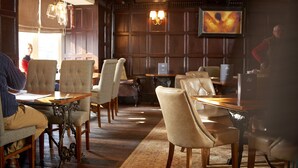 A restaurant with wooden paneling, cushioned chairs, and a chandelier. - Angel Inn Hotel (Pershore)