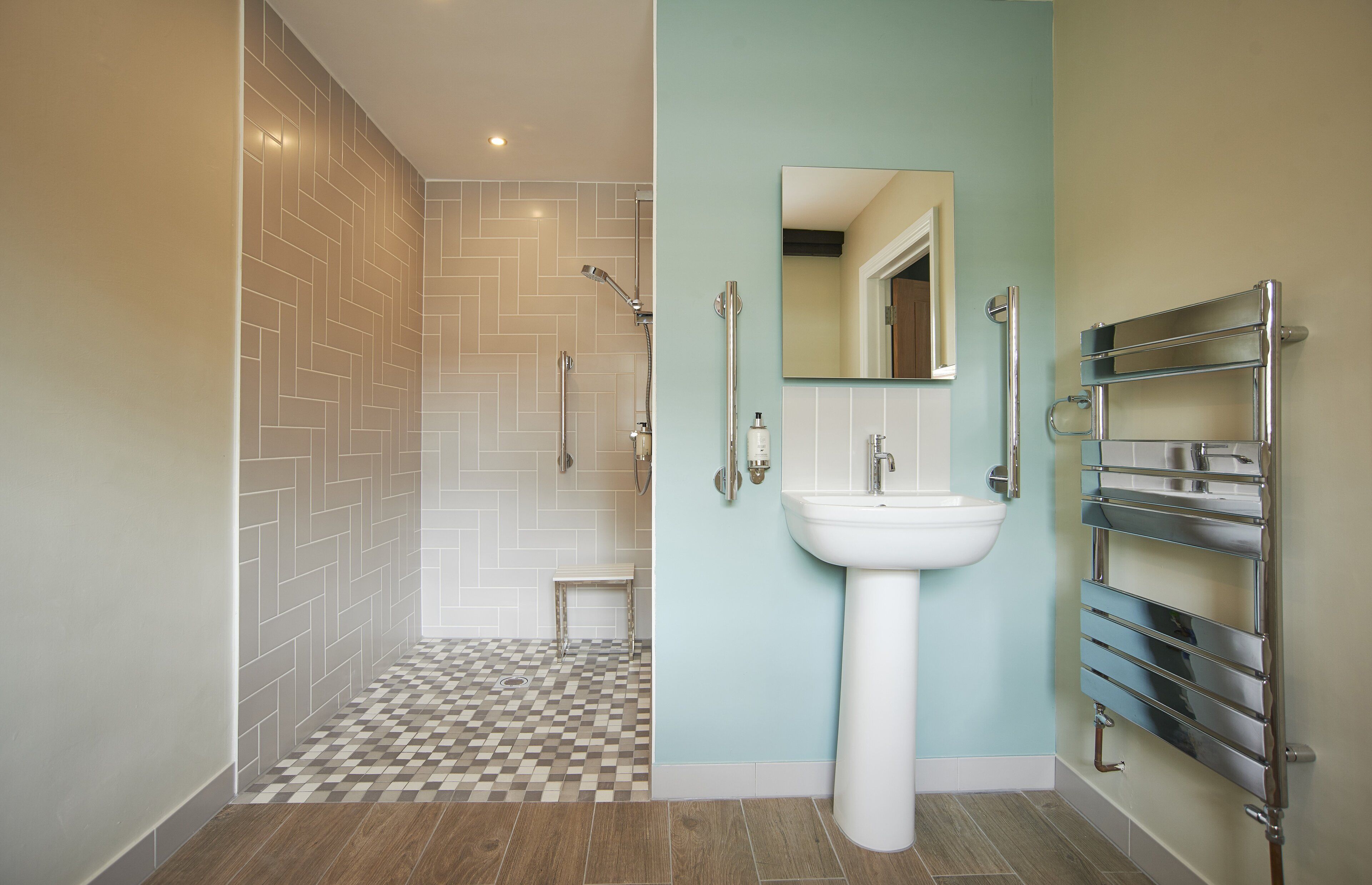 Un baño con ducha revestida de mosaico de espiga, lavamanos blanco y toallero cromado.