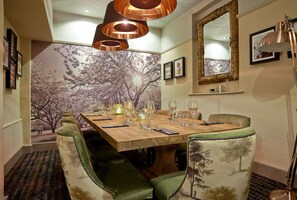 A dining area with a wooden table set for six, surrounded by upholstered chairs with a tree pattern. - Angel Inn Hotel (Pershore)