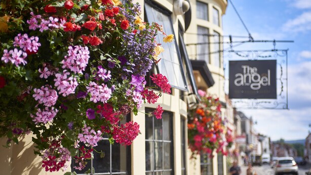 A building with a hanging flower display and a sign reading "The Angel". - Angel Inn Hotel (Pershore)