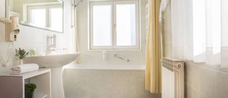 Een badkamer met een witte wastafel, een bad, een raam, een radiator en een zwart-wit geruite vloer.