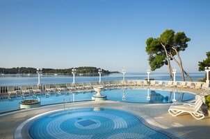 Un área de piscina con varias piscinas, sillones de descanso y vista al mar.