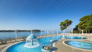 Uma área de piscina com uma fonte, espreguiçadeiras e vista para o mar.