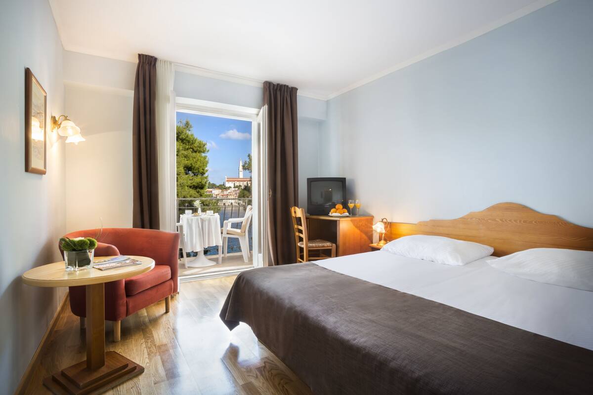 Habitación de hotel con cama, escritorio, silla, una mesita con planta y vistas al exterior.