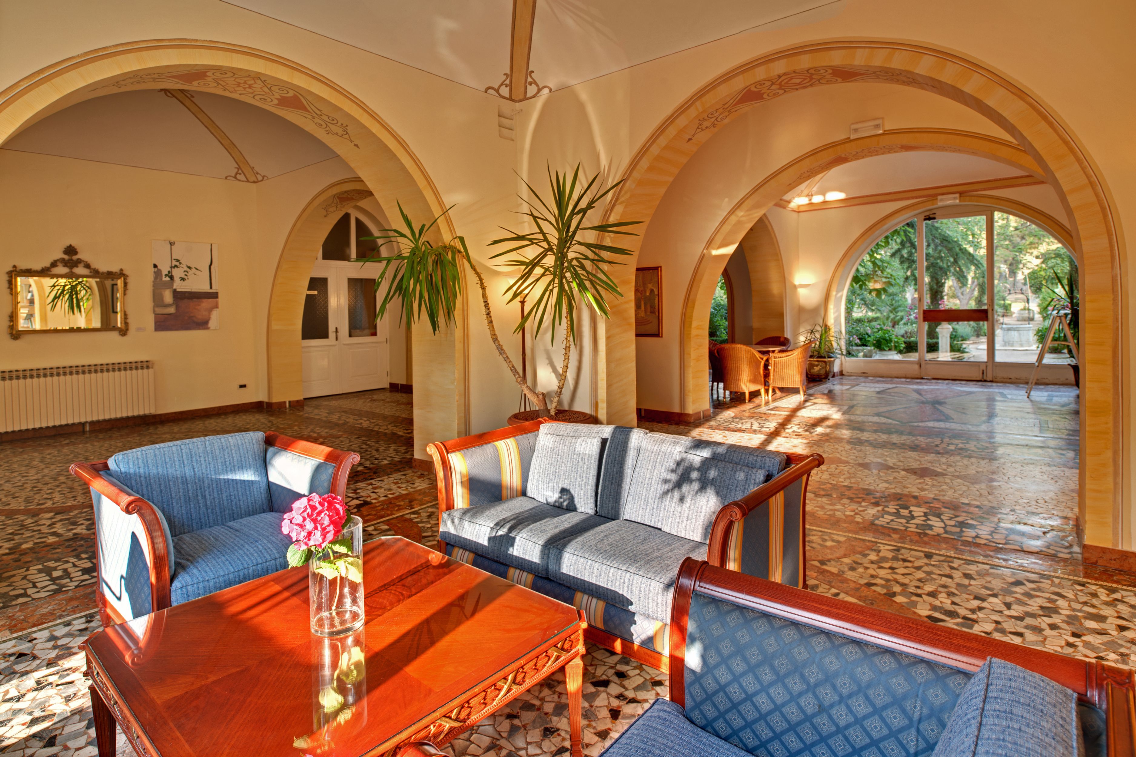A spacious lobby with a high ceiling, arched ceilings, and a tiled floor. There are two sofas and a wooden coffee table with a vase of flowers.