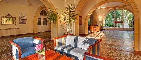 A spacious lobby with a high ceiling, arched ceilings, and a tiled floor. There are two sofas and a wooden coffee table with a vase of flowers.