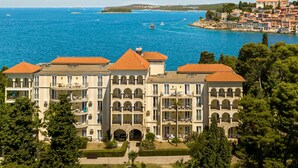 Um hotel grande, com vários andares e um pátio central, rodeado por vegetação exuberante e com vista para uma cidade costeira e o mar.