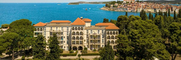 A large, multi-story hotel with a central courtyard, surrounded by lush greenery and overlooking a coastal town and the sea. - Maistra Select Island Hotel Katarina  (Rovinj)