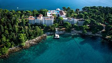An aerial view of a coastal hotel with multiple buildings, a swimming pool, and a boat docked near the shore.