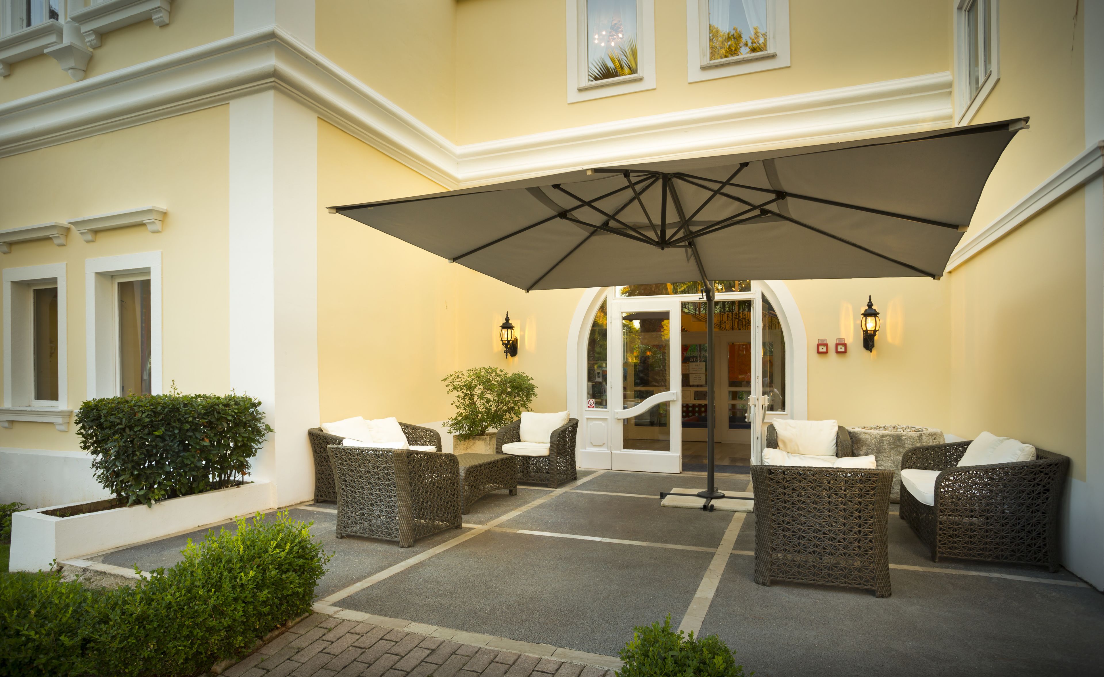 A patio area with wicker furniture, a large umbrella, and a building entrance.