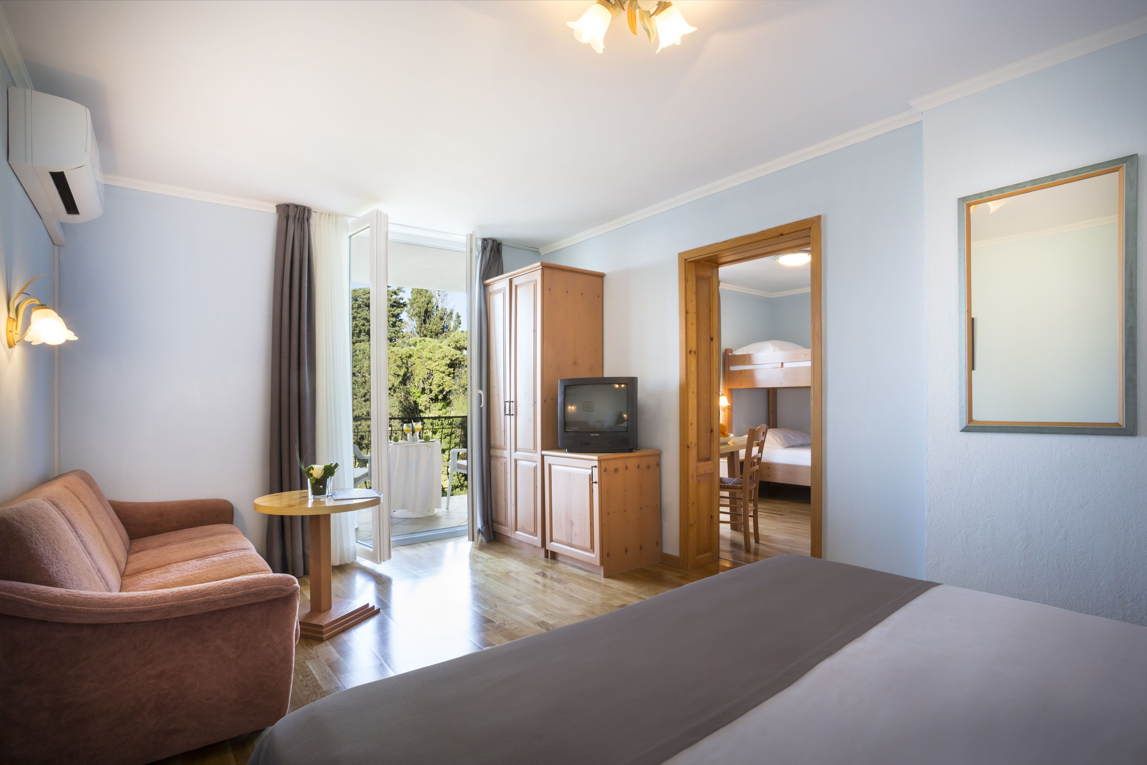 Une chambre d’hôtel avec un lit, un canapé, une télévision, une petite table avec une lampe et une vue sur l’extérieur.
