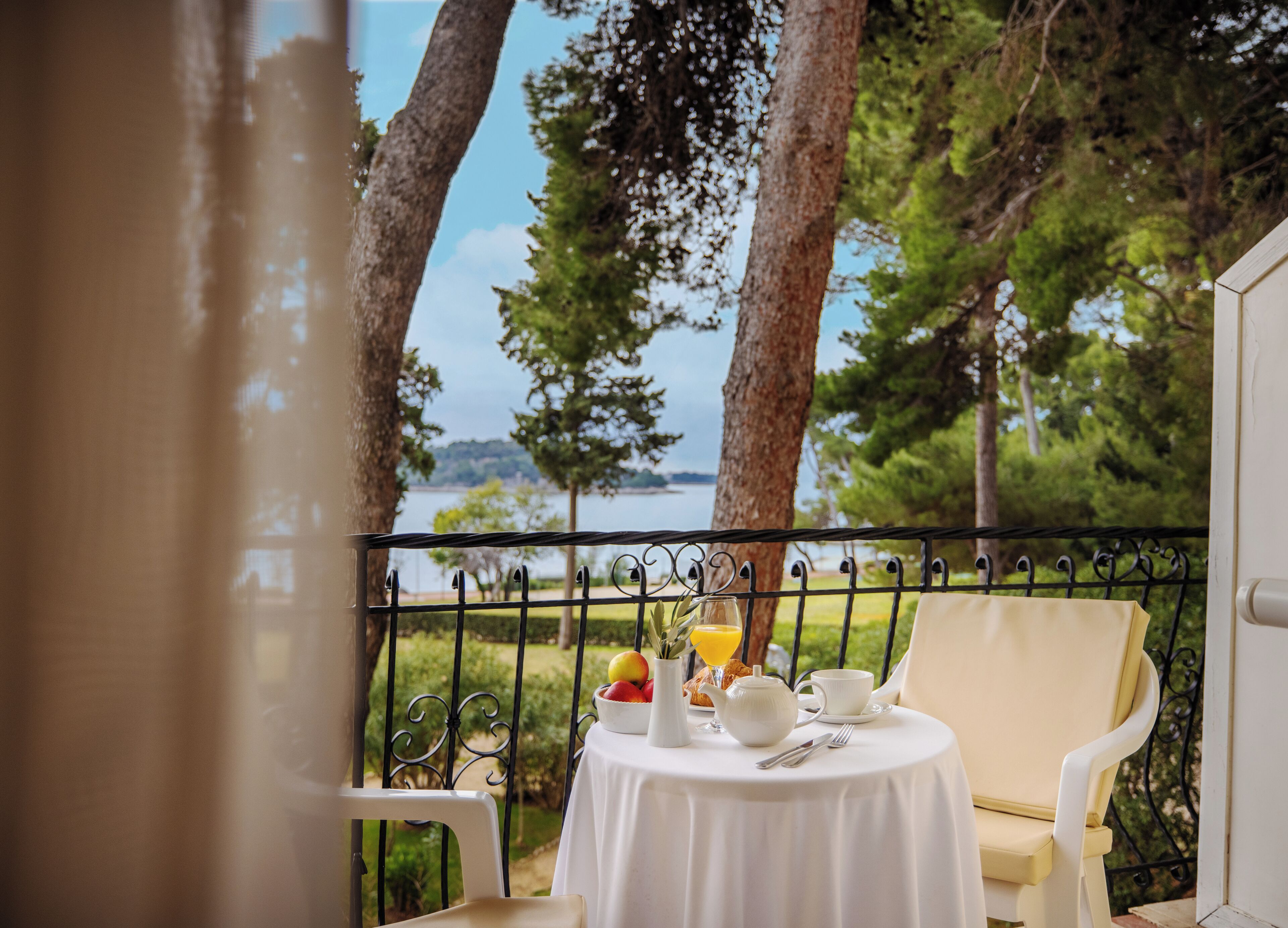 A balcony with a table set for breakfast, overlooking a lake and trees.