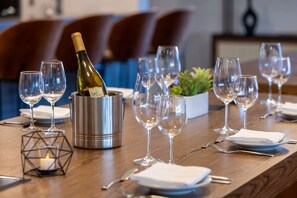 Una mesa de comedor dispuesta con copas de vino, una botella de champán y una vela en un soporte geométrico.