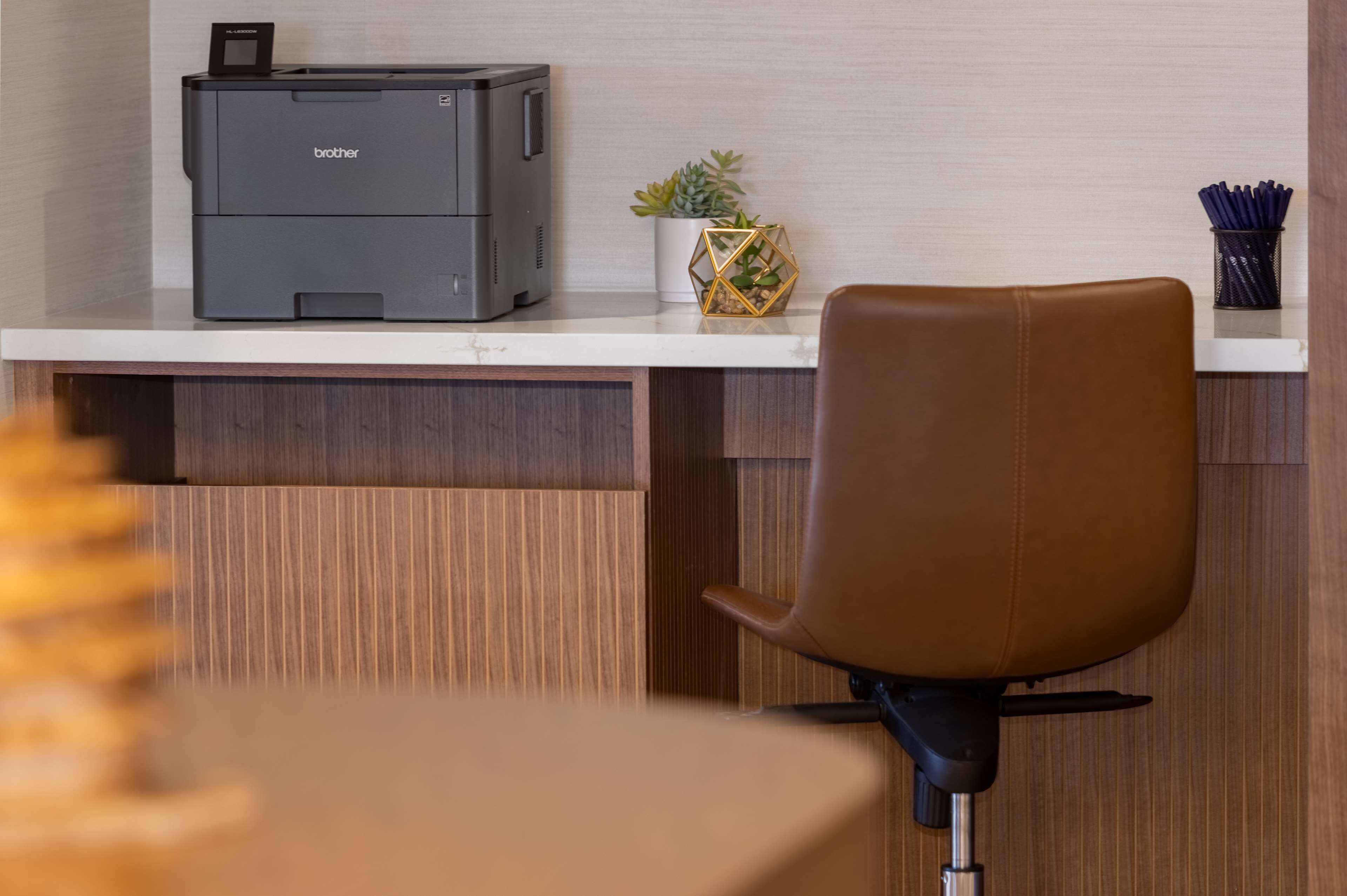 A modern office desk with a Brother printer, a potted plant, and a brown leather chair.